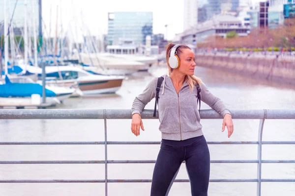 En atletisk kvinna som lyssnar på musik bredvid broräcket — Stockfoto