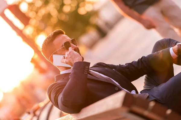 Un hombre de negocios sentado en un banco y hablando por teléfono —  Fotos de Stock