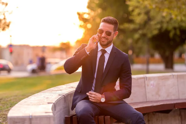 Un uomo d'affari seduto su una panchina e che parla al telefono — Foto Stock