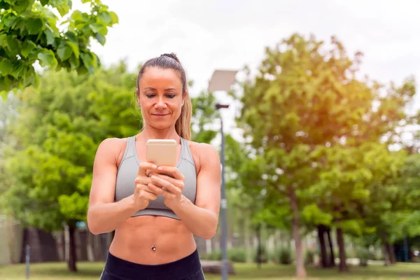 En atletisk kvinna som använder sin smartphone i parken — Stockfoto