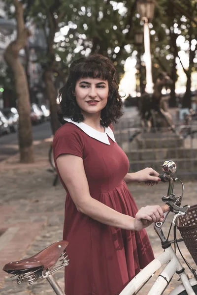 Uma mulher sorridente em um vestido vermelho com uma bicicleta — Fotografia de Stock