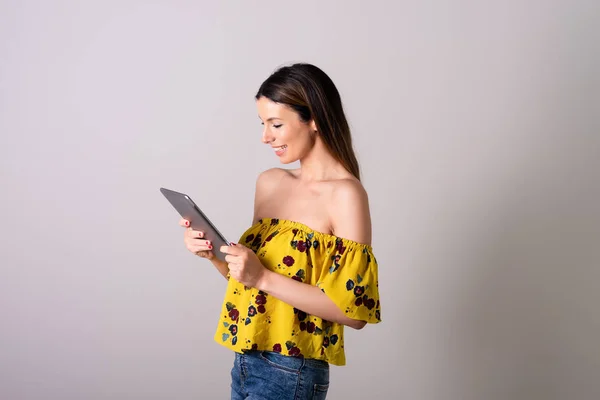 Uma jovem mulher feliz em um vestido amarelo usando um tablet — Fotografia de Stock