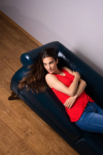 En allvarlig ung kvinna som ligger på en soffa — Stockfoto