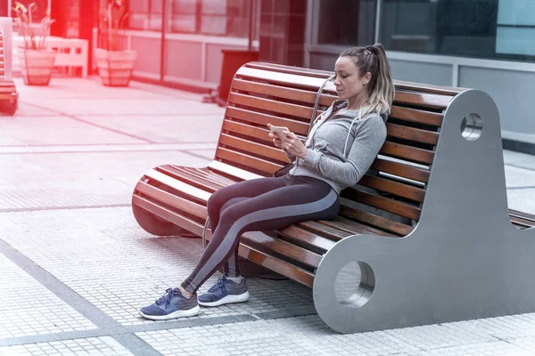 En atletisk kvinna sitter på en bänk och använda sin smartphone — Stockfoto