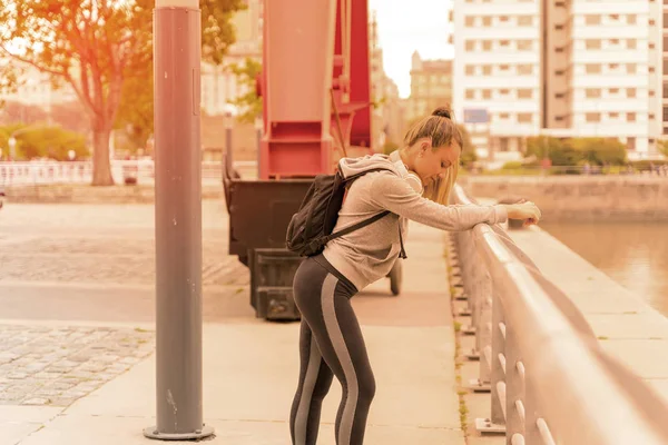 En atletisk kvinna vilar och lutar sig mot bron räcke — Stockfoto