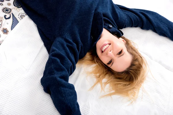 Una giovane donna sorridente sdraiata su un letto con un maglione — Foto Stock