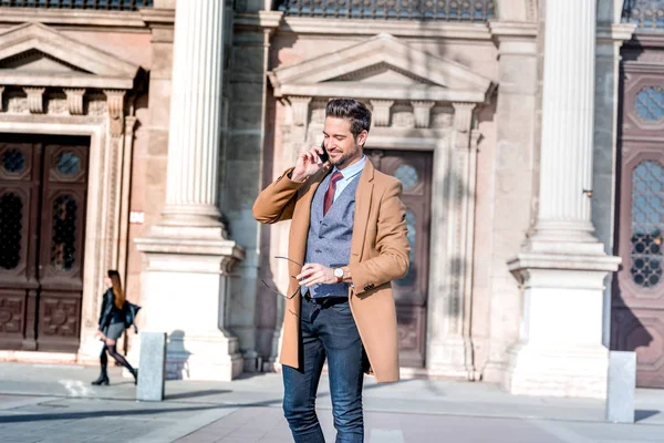 Een elegante man die op een plein staat en met zijn telefoon praat. — Stockfoto