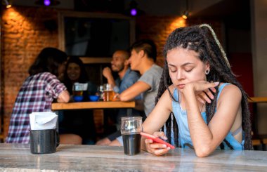 A girl alone with her phone in a bar clipart