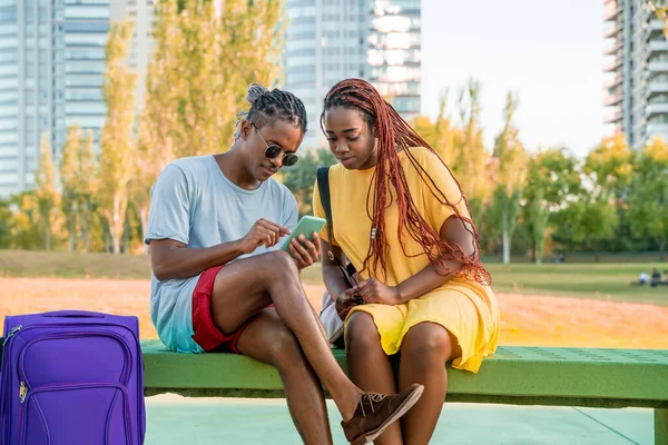 Um casal viajante usando um aplicativo em um telefone celular em um parque . — Fotografia de Stock