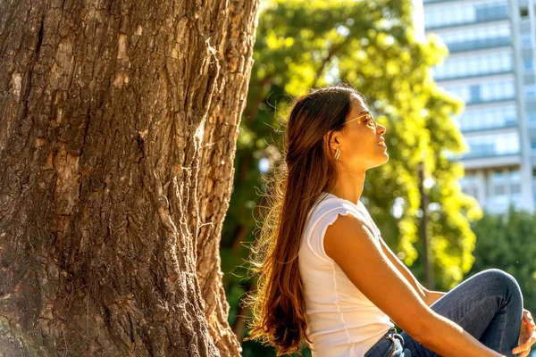 一个年轻的女人坐在一棵树旁享受阳光 — 图库照片