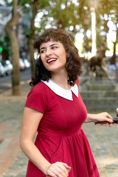 Une femme souriante dans une robe rouge avec un vélo — Photo