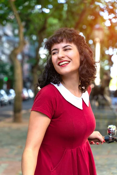 Una donna sorridente in un abito rosso con una bicicletta — Foto Stock