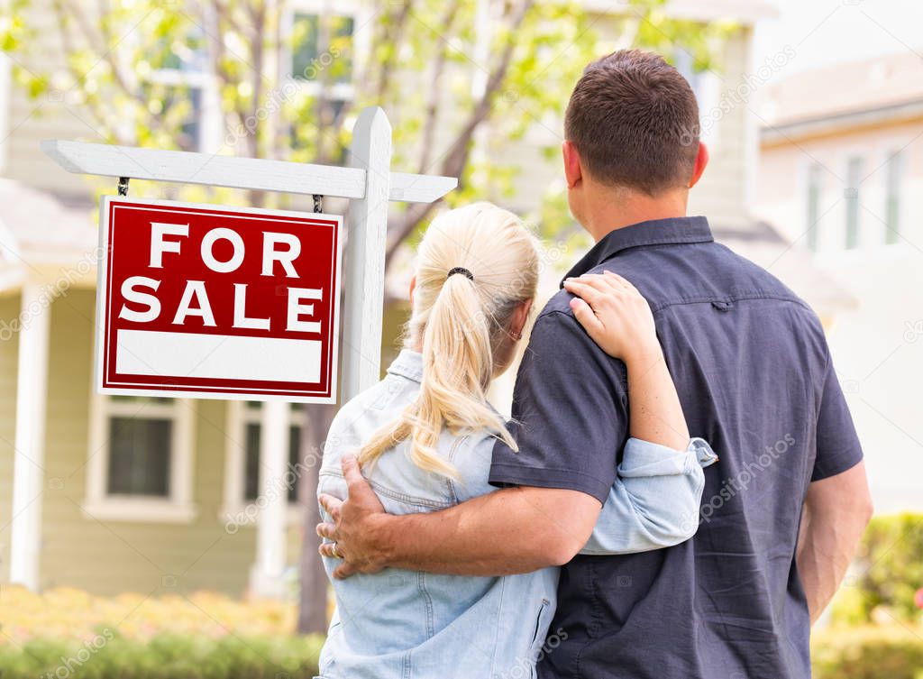 Caucasian Couple Facing Front of Sold Real Estate Sign and House.