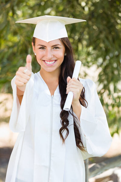 Mixed Race Thumbs Up Girl Celebrating Graduation Outside In Cap and Gown with Diploma in Hand.
