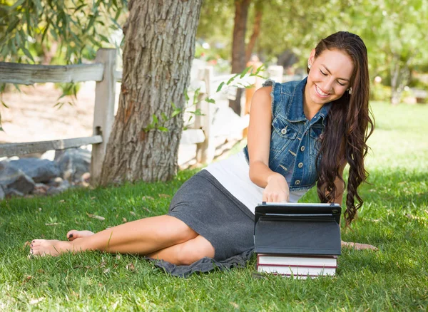 快乐混合的种族年轻女学生与书使用计算机片剂在外面坐在草 — 图库照片