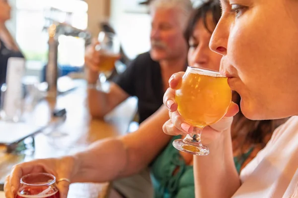 Female Sipping Glass of Micro Brew Beer At Bar With Friends.