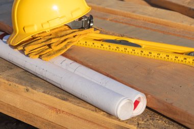 Ahşap plakalar üzerinde dinlenme soyut inşaatı baret, eldiven, seviyesi ve ev planları.