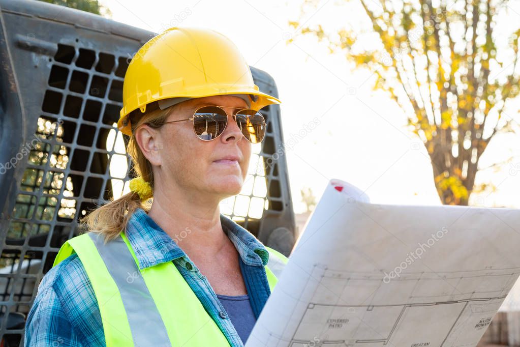 Female Worker Holding Technical Blueprints Near Small Bulldozer At Constrcution Site