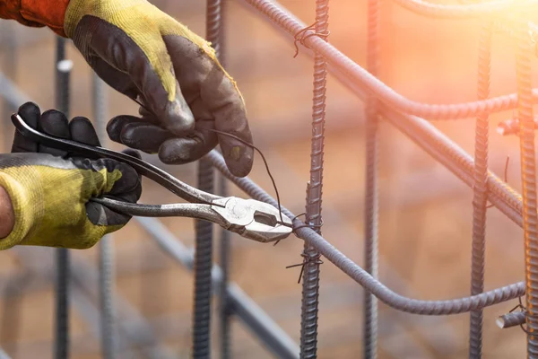 Worker Securing Steel Rebar Framing With Wire Plier Cutter Tool At Construction Site.