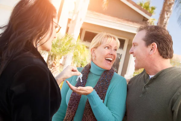 家の前に幸せなカップルに新しい家の鍵を引き渡すヒスパニックの女性の不動産エージェント — ストック写真