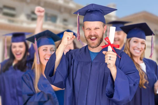Büszke férfi diplomás a kupakot és a ruháját előtt más diplomások — Stock Fotó