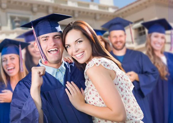 Büszke férfi diplomás a kupakot és a ruháját a lány között más diplomások mögött — Stock Fotó