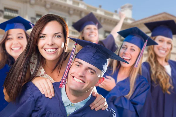 Stolzer männlicher Absolvent in Mütze und Kleid mit Mädchen unter anderen Absolventen dahinter — Stockfoto