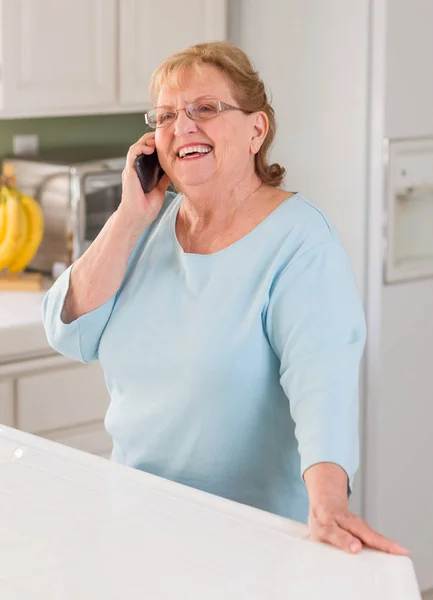 Mulher adulta sênior feliz em seu telefone celular inteligente na cozinha — Fotografia de Stock