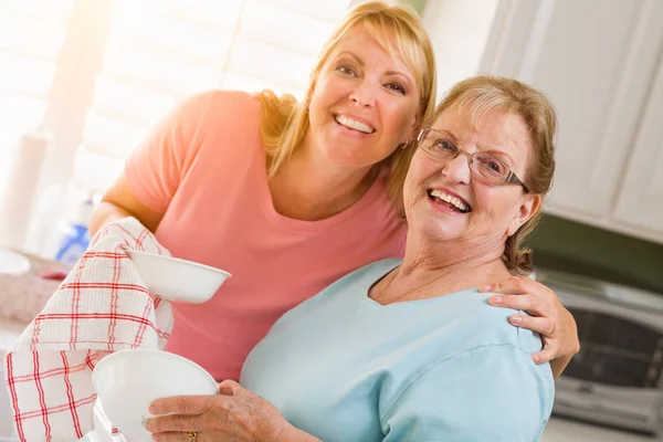Portrait of Smiling Senior Adult Woman and Young Daughter At Sink in Kitchen. — Stock Photo, Image