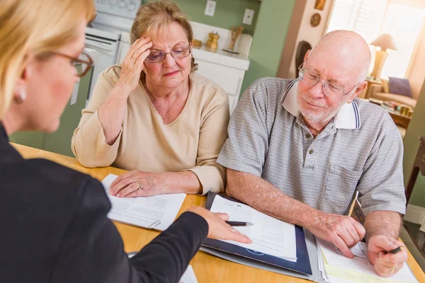 Senior volwassen paar gaan over documenten in hun huis met agent bij de ondertekening. — Stockfoto