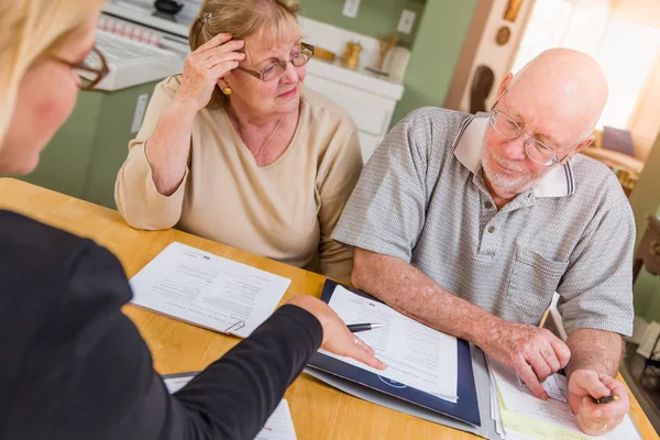 Senior vuxen par går över dokument i deras hem med agent vid undertecknandet. — Stockfoto