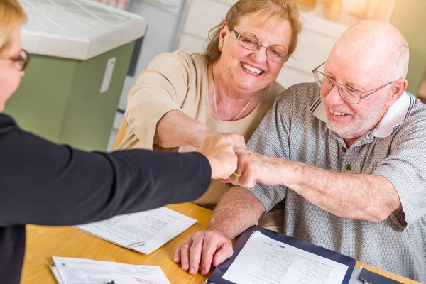 Senior volwassen paar vieren met vuist hobbel over documenten in hun huis met agent bij ondertekening. — Stockfoto