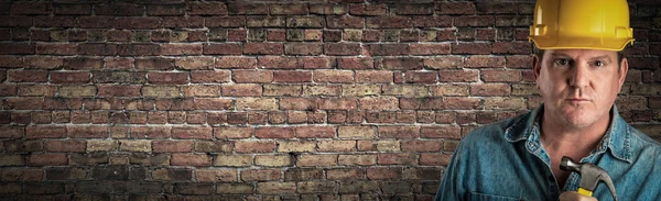 Male Contractor In Hard Hat Holding Hammer In Front Of Old Brick Wall Banner with Copy Space