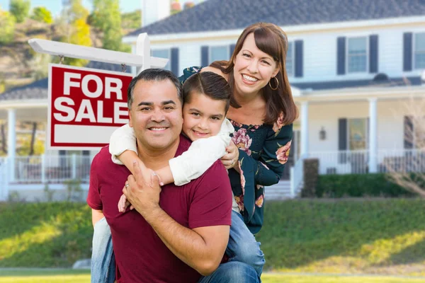 Feliz família de raça mista na frente da casa e para venda sinal imobiliário . — Fotografia de Stock