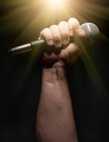 Microfone vertical preso firmemente no punho masculino em um fundo preto . — Fotografia de Stock