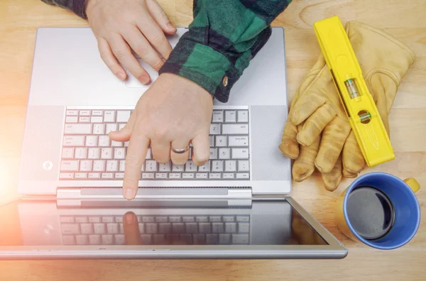 Werk handschoenen, niveau naast aannemer aanwijzen en beoordelingen project op laptop computer — Stockfoto