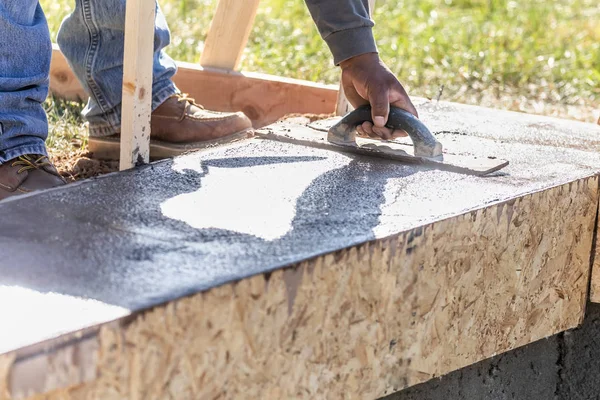 Travailleur de la construction utilisant une truelle en bois sur du ciment humide formant une capacité d'adaptation autour d'une nouvelle piscine — Photo