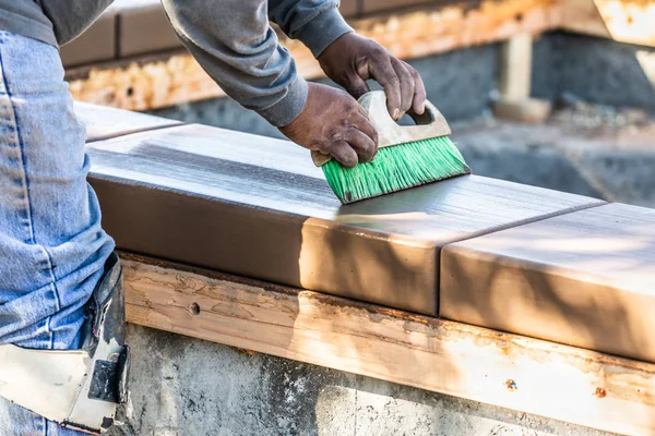 Trabalhador de construção usando escova em cimento molhado formando coping em torno de nova piscina — Fotografia de Stock