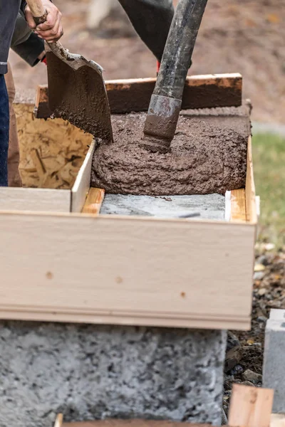 Trabajadores de la construcción vertiendo y nivelando cemento húmedo en el marco de madera — Foto de Stock