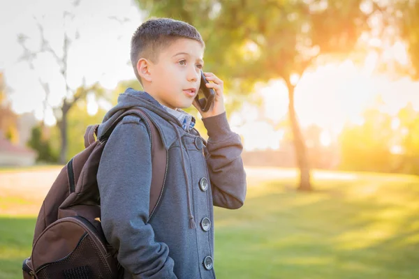 Joven chico hispano caminando al aire libre con mochila hablando por teléfono celular —  Fotos de Stock