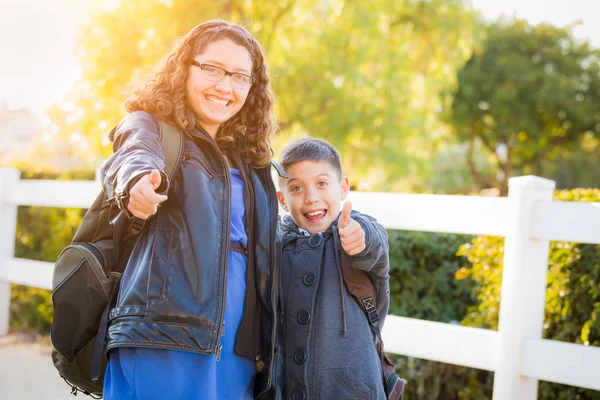 Irmão hispânico e irmã vestindo mochilas com polegares para cima — Fotografia de Stock