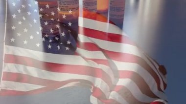 4k Slow Motion İlaç Şişeleri ve Hayalet Amerikan Bayrağı Dalgasıyla Düşen Haplar. İlaç şişesi etiketleri hayali isimler, adresler ve stok fotoğrafçılığı endüstrisi için özel olarak tasarlanmış bilgilerle tescilli değildir..