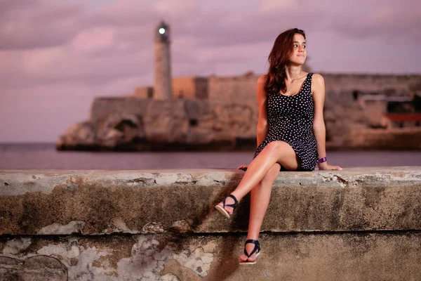 背景にエル モロ灯台とハバナ夕暮れマレコン護岸に座って美しいヒスパニック系の女の子 — ストック写真