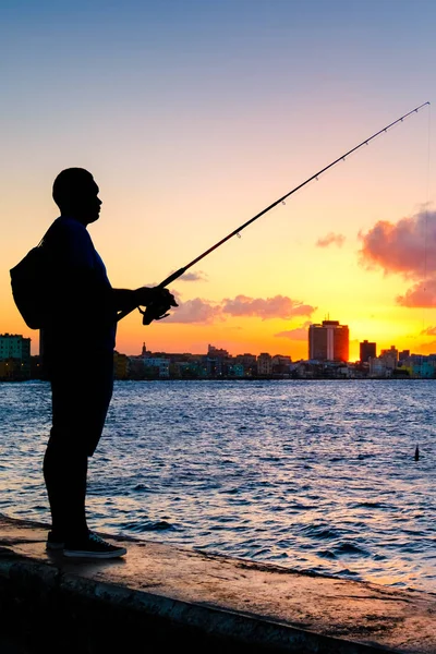 Silhouette of a man fishing on the bay of Havana at sunset with a view of the city skyline