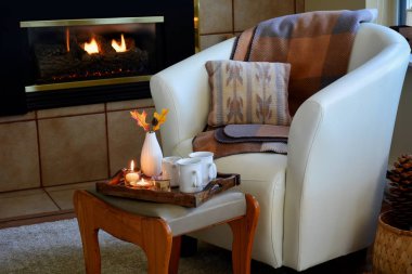 Yumuşak deri kova koltuk, mumlar, battaniye ve gaz şömine yanında çay Hygge ev rahatlığı. Doğal ışık yatay biçimi