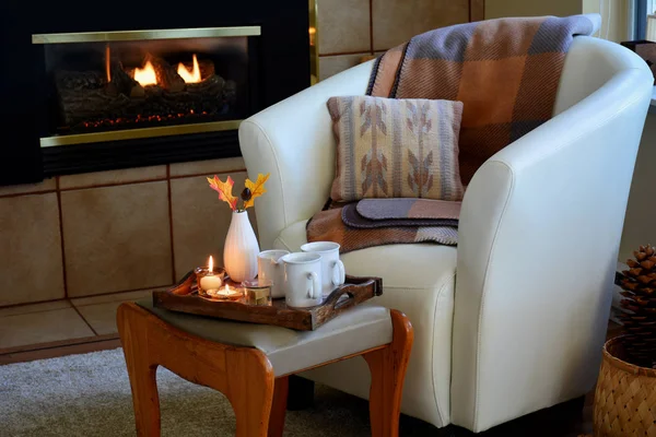 Yumuşak deri kova koltuk, mumlar, battaniye ve gaz şömine yanında çay Hygge ev rahatlığı. Doğal ışık yatay biçimi