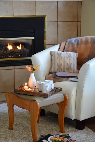Hygge home comfort with soft leather bucket chair, candles, blanket and tea beside gas fireplace.  Vertical format in natural light