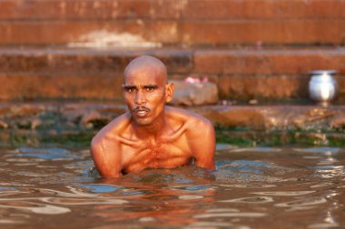 Ganj Nehri 'nin kutsal sularında oturan sıska kel adam. Varanasi, Hindistan 
