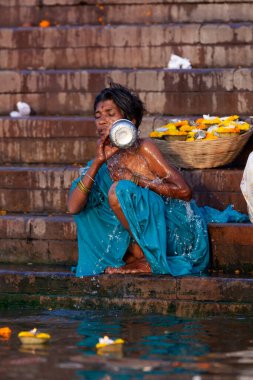 Mavi elbiseli bir kadın Ganj Nehri 'nin kutsal sularında gümüş bir kavanozda banyo yapıyor. Varanasi, Hindistan