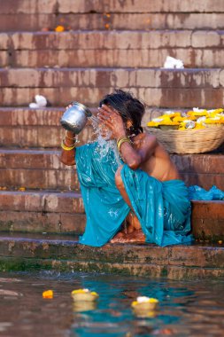 Mavi elbiseli bir kadın Ganj Nehri 'nin kutsal sularında gümüş bir kavanozda banyo yapıyor. Varanasi, Hindistan
